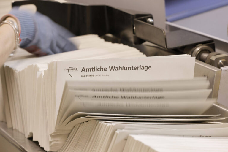 Mehrere Umschläge mit dem Aufdruck „Amtliche Wahlunterlage“ liegen in einer Maschine, daneben eine Hand mit Handschuh. Aufnahme aus Duisburg. Verdacht auf Wahlfälschung bei der Kommunalwahl in Duisburg-Marxloh sorgt für Ermittlungen gegen einen CDU-Kandidaten. Stapel von Wahlunterlagen in Duisburg: In Marxloh prüfen Ermittler Hinweise auf Stimmenkauf durch einen CDU-Kandidaten. Foto: IMAGO / biky