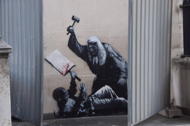 Banksys neues Gemälde: Mit Metallwänden verdeckt. Das Werk stellt einen Richter im traditionellen Gewand mit einer Allongeperücke dar, der einen auf dem Boden liegenden Protestierer zu erschlagen droht. Der Bedrohte hält ein blutüberströmtes Schild ohne Aufschrift. In Großbritannien findet derzeit eine Debatte über Zensur und Meinungsfreiheit statt. (Themenbild)