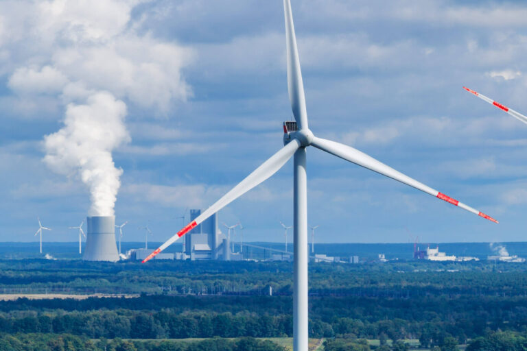 Im Vordergrund sieht man ein weiß-rotes Windrad, im Hintergrund raucht hingegen der Industriepark Schwarze Pumpe im brandenburgischen Proschim vor sich hin