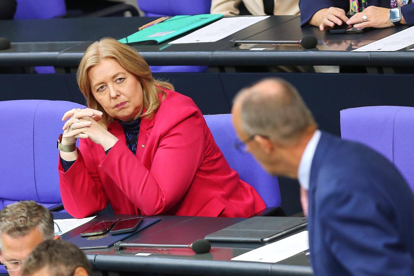 Eine Frau in rotem Blazer sitzt im Bundestag und blickt auf einen Mann im Vordergrund. Es handelt sich um Arbeitsministerin Bärbel Bas bei einer Plenarsitzung mit Kanzler Friedrich Merz. Aufnahme im September 2025 während der Haushaltswoche, im Kontext der geplanten Bürgergeld-Reform. Bundesarbeitsministerin Bärbel Bas im Bundestag: Die Sozialdemokratin will das Bürgergeld strenger regeln, Kanzler Merz drängt auf zügige Reform. Foto: IMAGO / dts Nachrichtenagentur