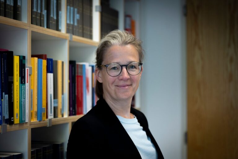Ann-Katrin Kaufhold, Professorin für Öffentliches Recht und SPD-Kandidatin für das Bundesverfassungsgericht, steht vor einem Bücherregal mit Fachliteratur. Sie trägt Brille, helles Oberteil und dunkles Jackett, schaut in die Kamera. Ann-Katrin Kaufhold: SPD-Kandidatin für Karlsruhe, von Plagiatsprüfer Weber wegen ihrer „Systemaufsicht“-Thesen kritisiert. Foto: LMU