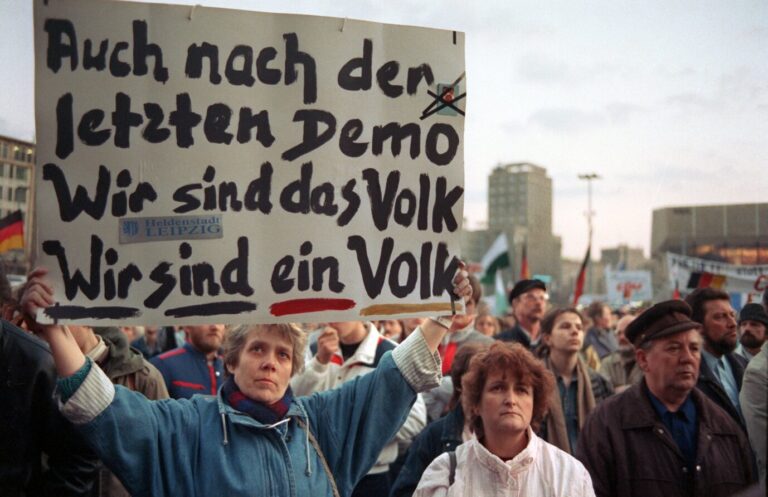 Deutsche demonstrieren und zeigen ein Transparent mit der Aufschrift „Auch nach der letzten Demo – Wir sind das Volk – Wir sind ein Volk" in Leipzig, 1990.