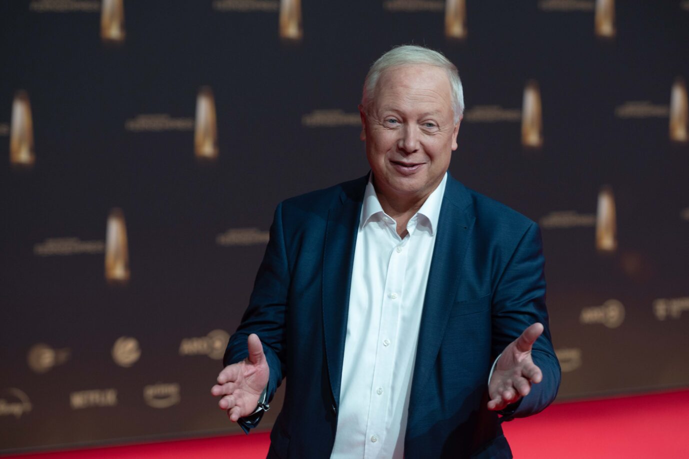 Der Ex-WDR-Intendant und Ex-ARD-Vorsitzende Tom Buhrow trägt einen Anzug, lächelt merwkürdig und streckt seine Hand in Richtung der Kamera – erneut ist er Spitzenverdiener im Rundfunk