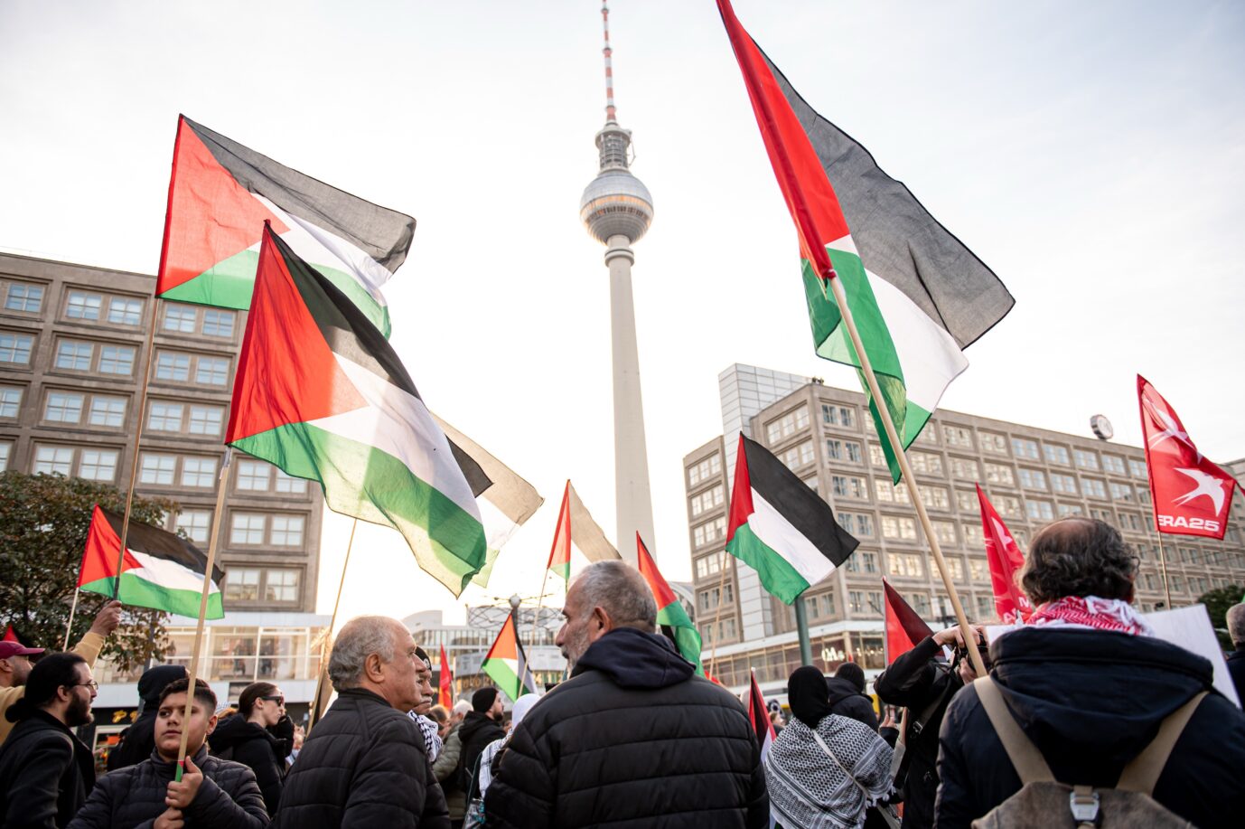Mehrere Personen mit palästinensischen Fahnen stehen auf dem Alexanderplatz in Berlin, im Hintergrund ist der Fernsehturm zu sehen. Das Foto zeigt eine frühere propalästinensische Demonstration am selben Ort, an dem am 7. Oktober erneut eine Kundgebung stattfinden soll. Teilnehmer mit palästinensischen Fahnen am Berliner Alexanderplatz: Dort ist am Montag eine propalästinensische Kundgebung geplant – dessen Absage wird von Israels Botschafter in Deutschland gefordert. Foto: picture alliance/dpa | Fabian Sommer