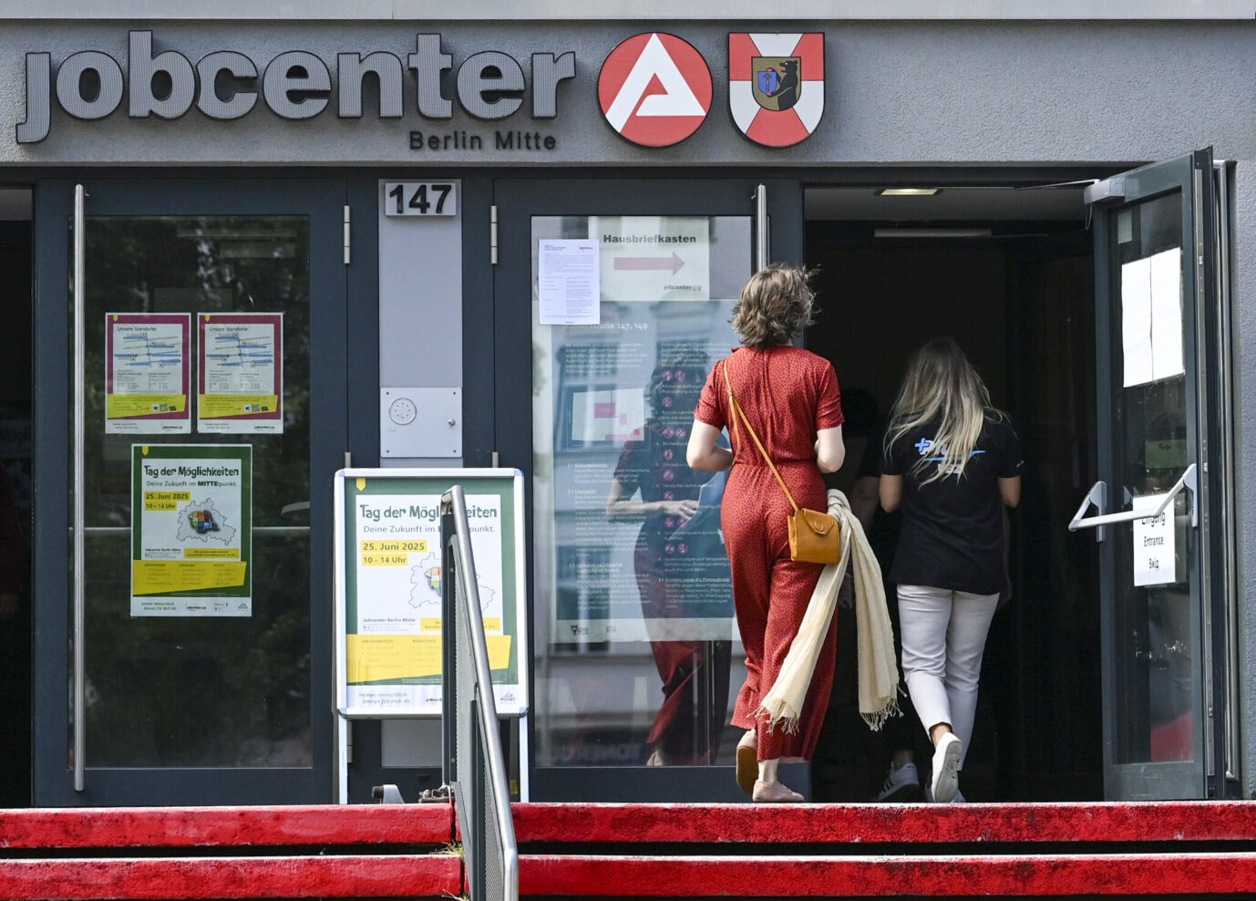 Man sieht den Eingang des Jobcenters in Berlin-Mitte, eine Frau in roter Kleidung geht hinein – Symboldbild für Schuldenfalle und Bürgergeld
