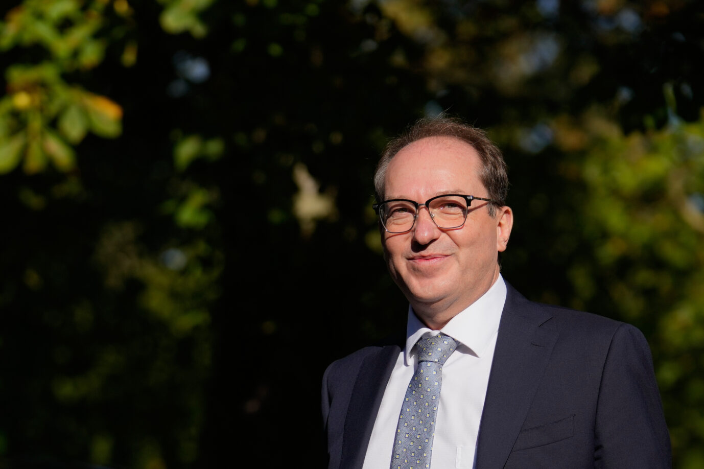 Mann im Anzug mit Brille im Freien, lächelt in die Kamera. Er steht für die aktuelle Debatte um die staatliche Finanzierung der Amadeu-Antonio-Stiftung. Alexander Dobrindt: Der Innenminister führt die staatliche Förderung der Amadeu-Antonio-Stiftung fort. Foto: picture alliance / ASSOCIATED PRESS | Ebrahim Noroozi