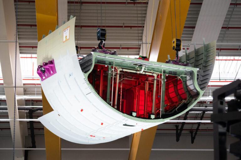 Ein großes gebogenes Metallbauteil hängt an einem gelben Hallenkran, im Innern sind Leitungen und Verstrebungen sichtbar. Das Bauteil ist Teil des Treibstofftanks für das Airbus-Langstreckenmodell A321 XLR, aufgenommen bei der Eröffnung der neuen Produktionshalle in Augsburg. Ein Flugzeugbauteil in einer Produktionshalle: Die deutsche Industrie meldet im August erneut weniger Aufträge. Foto: picture alliance / CHROMORANGE | Michael Bihlmayer