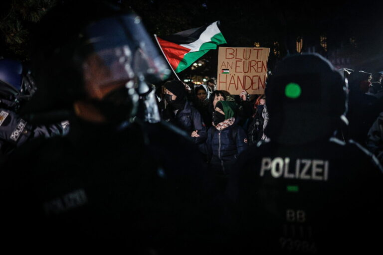 Mehrere Polizisten in Schutzkleidung beobachten eine Gruppe von Demonstranten, die Palästinafahnen schwenken und ein Schild mit der Aufschrift „Blut an euren Händen“ hochhalten. Die Szene zeigt eine verbotene Pro-Hamas-Kundgebung in Berlin, die trotz Versammlungsverbot rund 500 Teilnehmer anlockte. Polizisten stehen einer Menge von Demonstranten mit Palästinafahnen gegenüber: Auf dem Berliner Alexanderplatz löst die Polizei eine verbotene Hamas-Kundgebung auf. Foto: picture alliance / Sipa USA | SOPA Images