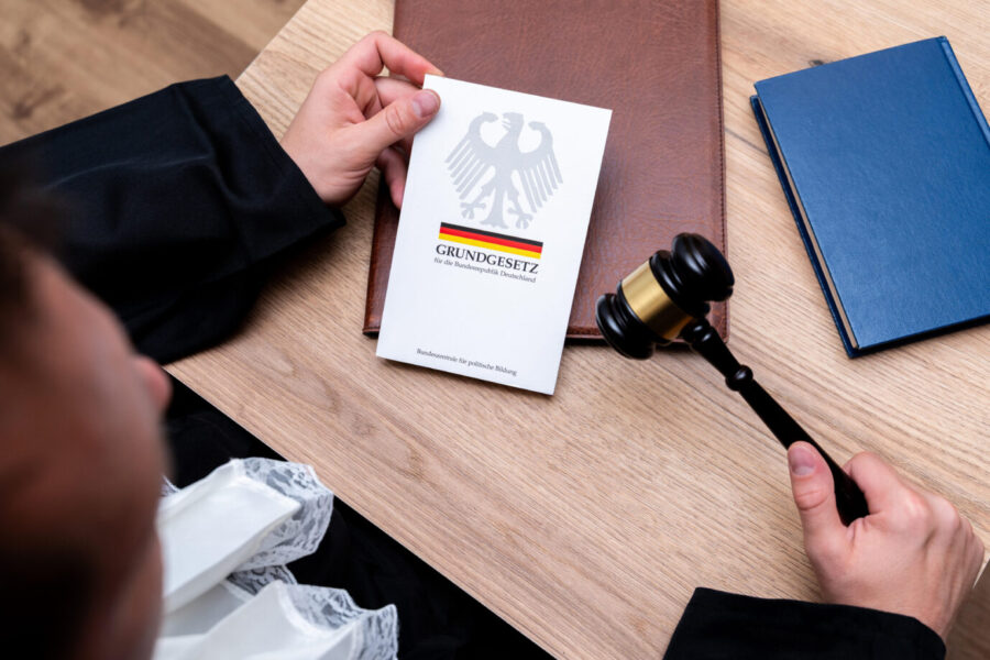 Das Bild zeigt einen Richter mit Richterhammer und dem Grundgesetz der Bundesrepublik Deutschland. Symbolfoto Rechtsstaat, Verfassung, Justiz, Demokratie und Gesetzgebung in Deutschland. Es ist ein Symbolbild für die Klimapolitik.