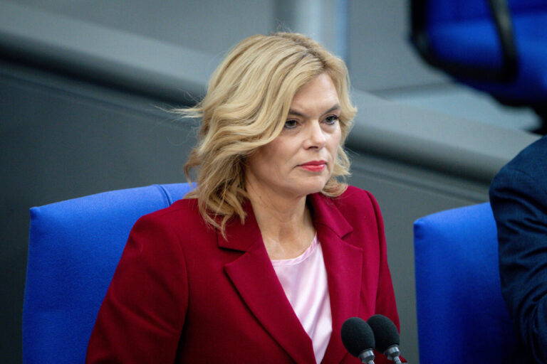 Julia Klöckner sitzt im Plenarsaal des Deutschen Bundestages an einem Mikrofonplatz, trägt ein rotes Jackett und blickt konzentriert nach vorn. Bundestagspräsidentin Julia Klöckner distanziert sich nach Abmahnung von Werbung der Weimer Media Group für den Ludwig-Erhard-Gipfel. Bundestagspräsidentin Julia Klöckner im Plenarsaal: Ihr Amt wurde ohne Zustimmung für Werbung genutzt. Foto: picture alliance / Flashpic | Jens Krick