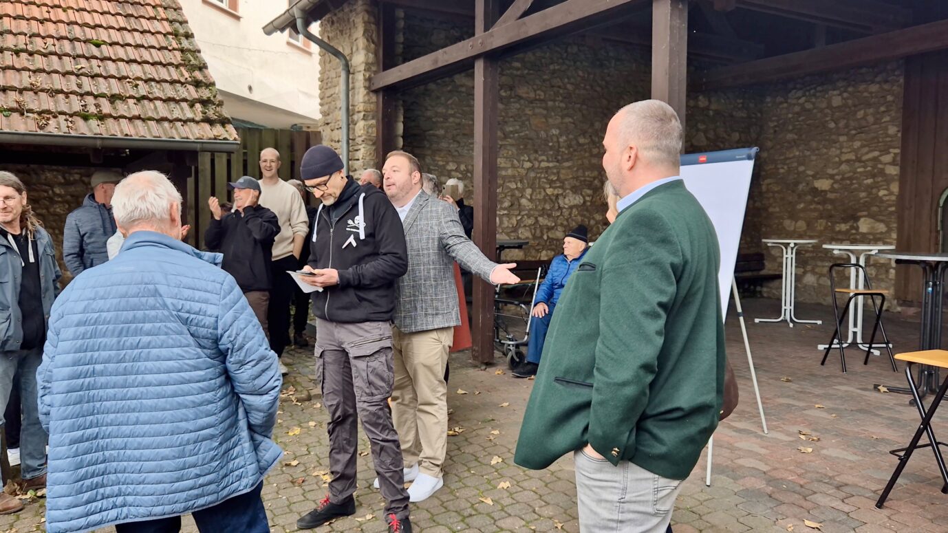 Zu sehen sind mehrere Personen während eines Wortwechsels auf dem Dorfplatz in Gauersheim, darunter Damian Lohr, Tilo Hausmann und Jürgen Wiedenhöfer. Das Foto entstand am 3. Oktober 2025 während des Bürgerdialogs, bei dem es laut Polizei zu verbalen und körperlichen Provokationen zwischen Teilnehmern kam. Auseinandersetzung auf dem Dorfplatz in Gauersheim: Linke behindern den AfD-Abgeordneten Damian Lohr. Foto: privat