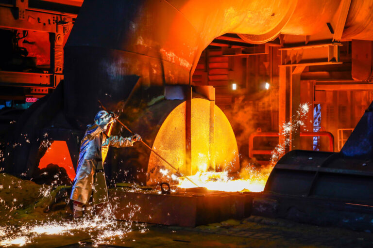 Ein Stahlarbeiter im Schutzanzug steht vor einer flammenden Maschine