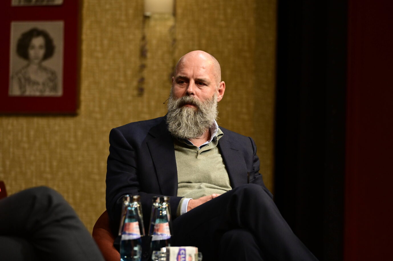 Mann mit grauem Vollbart sitzt auf einem Podiumsgespräch in einem Saal, trägt Sakko und Pullover. Vor ihm zwei Wasserflaschen auf dem Tisch. Veranstaltung im Gerhart-Hauptmann-Theater in Görlitz, 2024, über Meinungsvielfalt und Presselandschaft. Holger Friedrich beim Gespräch über Meinungsvielfalt in Görlitz: Mit dem „Projekt Halle“ will er neue Zeitungen im Osten gründen. Foto: IMAGO / pictureteam