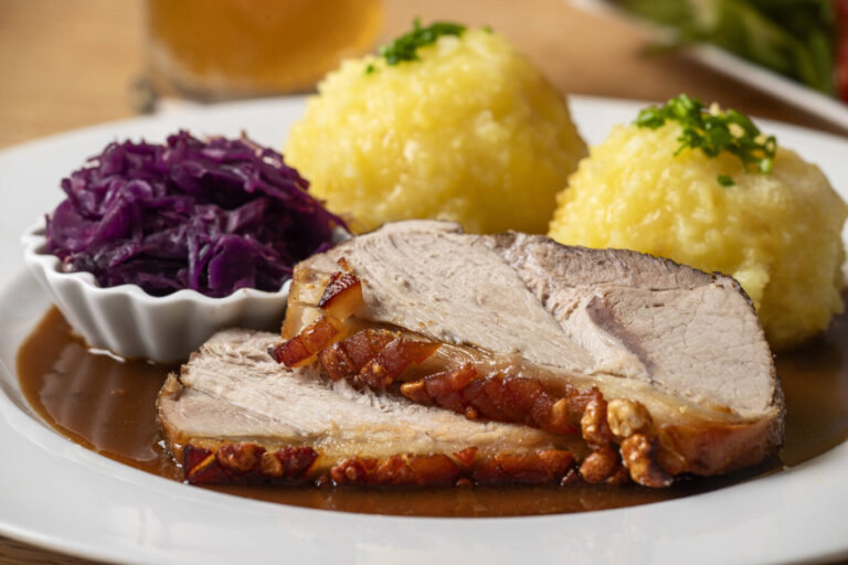 Auf einem Teller liegen ein Schweinebraten, Kartoffelknödel und ein Schälchen mit Rotkohl, dazu braune Soße – in der Gastronomie ist das wieder im Trend