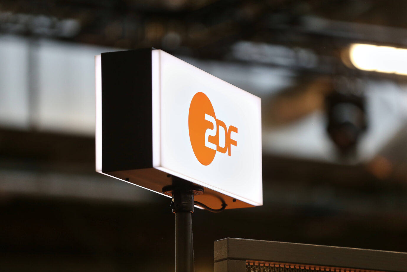 Ein beleuchtetes ZDF-Logo auf einem schwarzen Sockel, aufgenommen in einem Fernsehstudio mit unscharfem Hintergrund. Das Bild zeigt das Markenzeichen des Senders, der wegen des Falls des Reporters Andreas Halbach in der öffentlichen Diskussion steht. ZDF-Logo bei der Digitalmesse „Re:publica“: Ein Reporter erhebt schwere Vorwürfe gegen seinen Arbeitgeber. Foto: IMAGO / dts Nachrichtenagentur