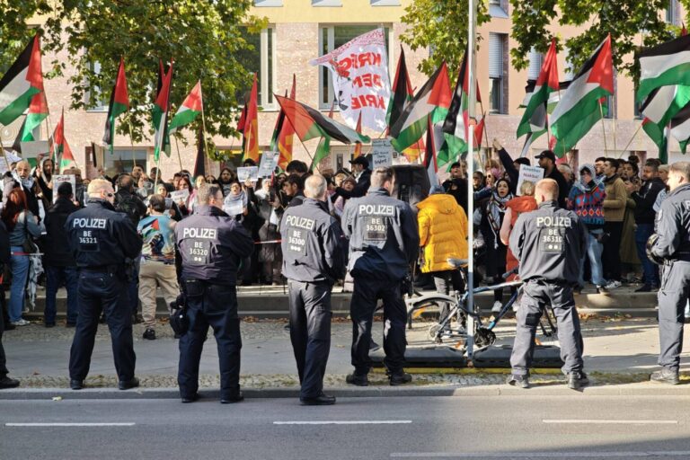 Mehrere Berliner Polizisten stehen vor einer Menschenmenge mit palästinensischen Fahnen und Transparenten. Das Foto zeigt eine propalästinensische Demonstration in Berlin, während die Polizei eine geplante Hamas-Demo am Alexanderplatz verbietet. Berliner Polizisten sichern eine propalästinensische Demonstration: Die Hamas-Kundgebung am 7. Oktober wird untersagt. Foto: IMAGO / dts Nachrichtenagentur
