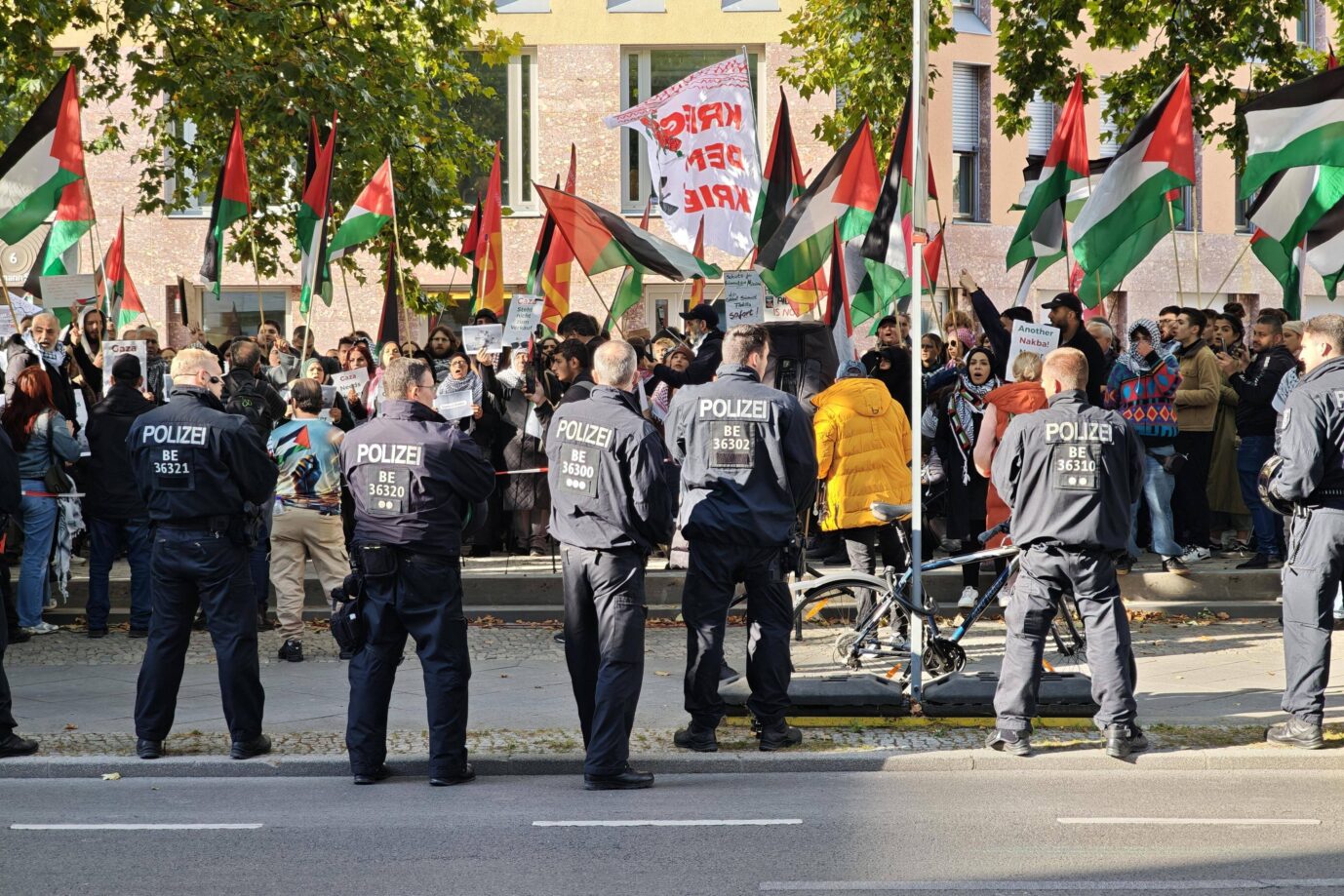 Mehrere Berliner Polizisten stehen vor einer Menschenmenge mit palästinensischen Fahnen und Transparenten. Das Foto zeigt eine propalästinensische Demonstration in Berlin, während die Polizei eine geplante Hamas-Demo am Alexanderplatz verbietet. Berliner Polizisten sichern eine propalästinensische Demonstration: Die Hamas-Kundgebung am 7. Oktober wird untersagt. Foto: IMAGO / dts Nachrichtenagentur