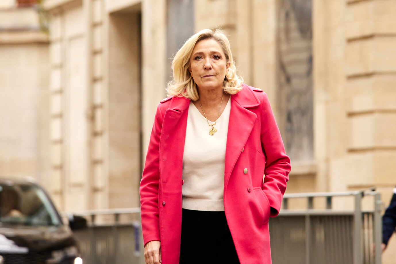 Die Fraktionsvorsitzende des Rassemblement National, Marine Le Pen trägt eine rote Jacke und läuft mit selbstbewußtem Gesichtsausdruck auf die Kamera zu