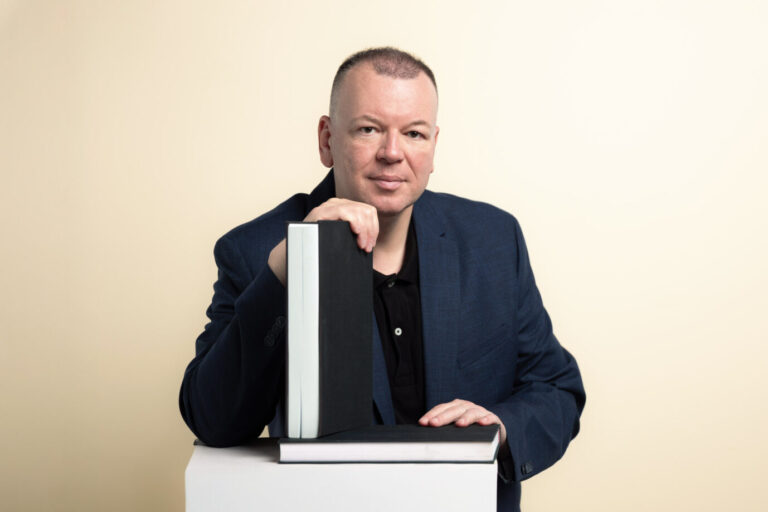 Der Kommunikationswissenschaftler Stefan Weber sitzt an einem Tisch und stützt sich auf zwei Bücher. Er wirft der Weimer Media Group vor, seine Texte ohne Zustimmung auf The European veröffentlicht zu haben. Stefan Weber in seinem Porträt: Der Wiener Plagiatsforscher ließ den Verlag von Kulturstaatsminister Wolfram Weimer abmahnen. Foto: Joachim Bergauer