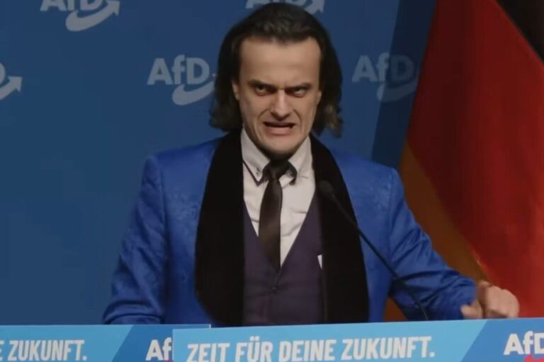 Ein Man mit schulterlangen dunklen Haaren schaut wahnsinnig drein und steht an einem Rednerpult: es ist der mysteriöse (noch)-AfD-Kandidat Alexander Eichwald während seiner Rede