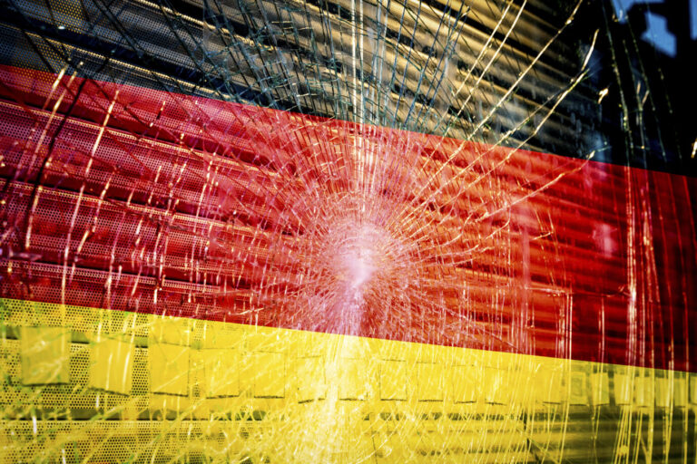 Deutschland-Fahne bzw. Flagge vor zerschlagener Scheibe. Symbolisch für deutsche Wirtschaft in Scherben, durch Entlassungen, Abwanderung, Stellenstreichungen und Insolvenzen von großen Unternehmen. FOTOMONTAGE