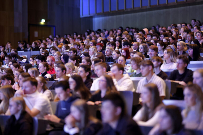 Großer, gut gefüllter Hörsaal mit dicht gedrängt sitzenden Studenten, die nach vorn blicken; viele junge Erwachsene, gemischte Gruppen, konzentrierte Atmosphäre. Studie zu Sanktionen gegen konservative Vorträge und zum Umgang mit kontroversen Positionen an Universitäten.