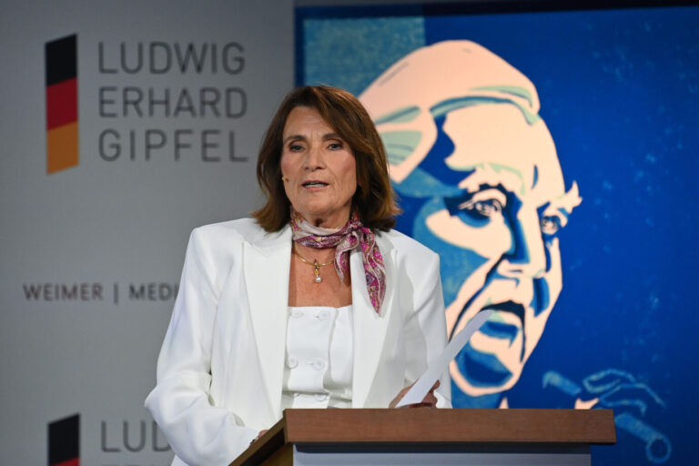 Christiane Götz-Weimer steht während eines Ludwig-Erhard-Gipfels vor einem Rednerpult – vielleicht um gerade Politiker und Finanzbosse miteinander zu verkuppeln