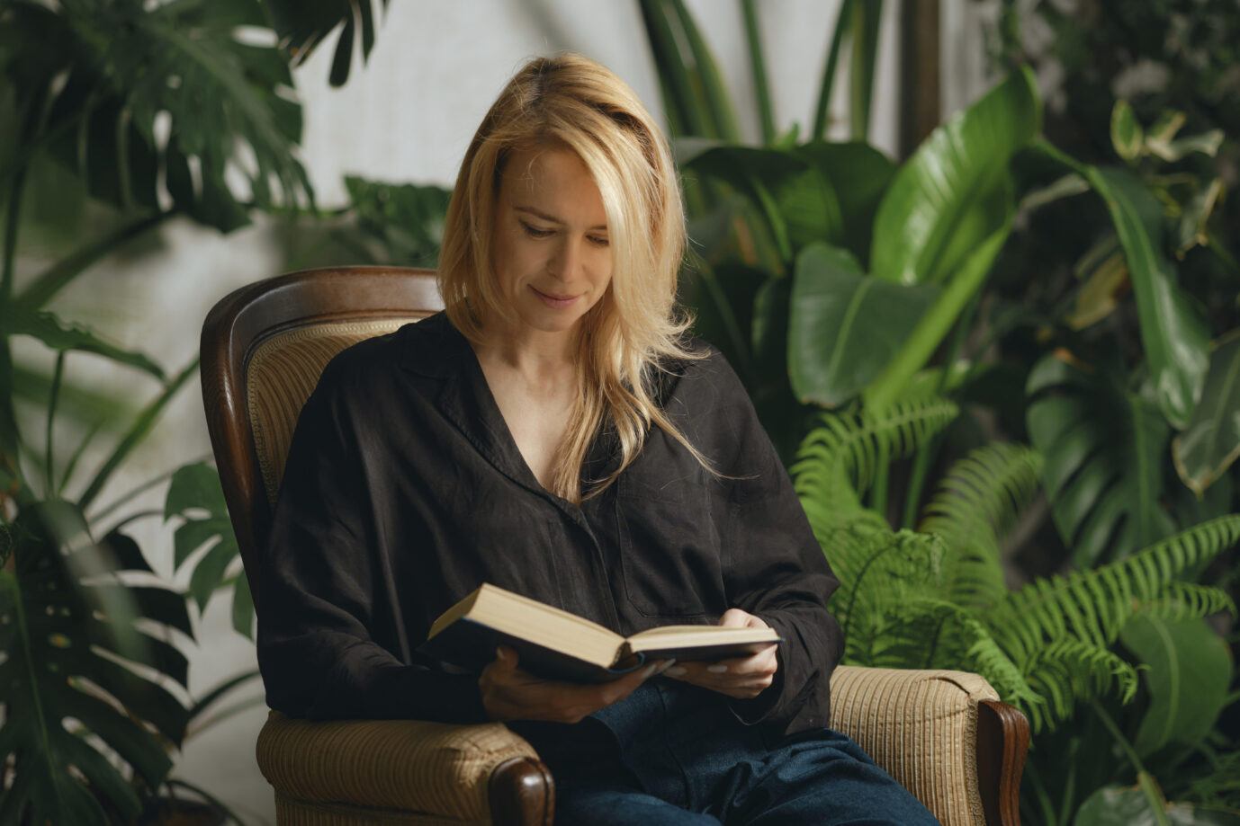 Eine Frau liest ein Buch in ihrem Wohnzimmer (Symbolbild): Vor allem in den Jahrgängen ab 1980 vorwärts erfreut sich „Spicy Dark Romance“ großer Beliebtheit. Frauenliteratur, die einst als Groschenromane bekannt war. (Themenbild)