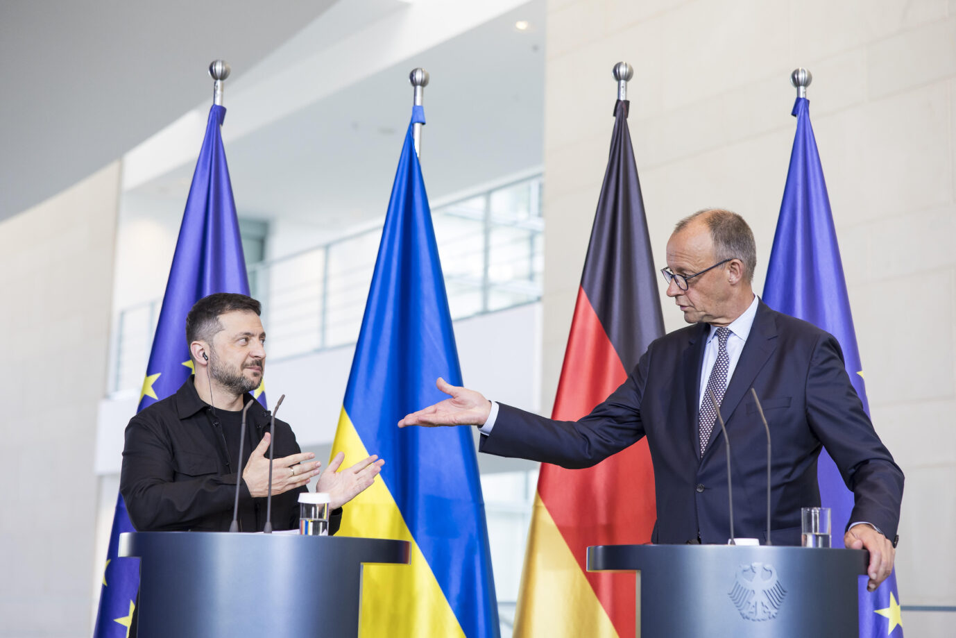 Ukraines Präsident Wolodymyr Selenskij und Bundeskanzler Friedrich Merz stehen bei einer gemeinsamen Pressekonferenz am Rednerpult, flankiert von den Flaggen der Europäischen Union, der Ukraine und Deutschlands, und gestikulieren einander zu. Treffen im Kanzleramt, bilaterale Konsultationen zu Sicherheitsfragen und aktueller Ukraine-Politik. Ukraines Präsident Selenskij bei Bundeskanzler Friedrich Merz: „Unveränderte und volle Unterstützung“ für Kiew. Foto: picture alliance / PIC ONE | Ben Kriemann