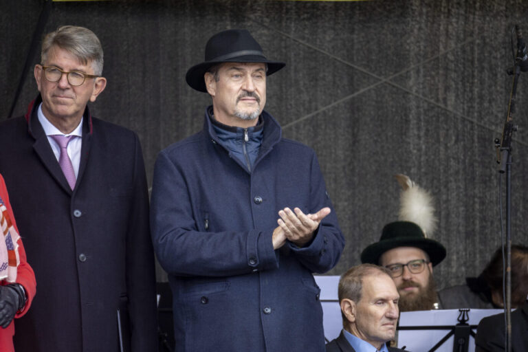 Bayerns Ministerpräsident Markus Söder (CSU) trägt eine dunkle Jacke und schaut mit ernstem Blick in die Ferne, daneben steht Kulturstaatsminister Wolfram Weimer und schaut bedrückt