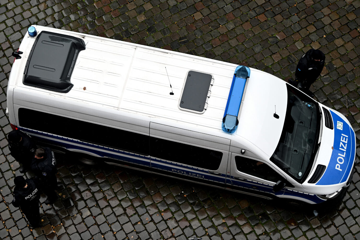 Ein Einsatzfahrzeug der Berliner Polizei steht auf nassem Kopfsteinpflaster, mehrere Beamte stehen daneben. Das Bild zeigt den Polizeieinsatz im Zusammenhang mit der Festnahme eines Syrers, der einen Anschlag in Berlin vorbereitet haben soll. Polizeifahrzeug in Berlin: Beamte nahmen am Sonnabend einen 22jährigen Syrer fest, der laut Ermittlern einen Anschlag geplant haben soll. Foto: picture alliance/dpa | Lilli Förter
