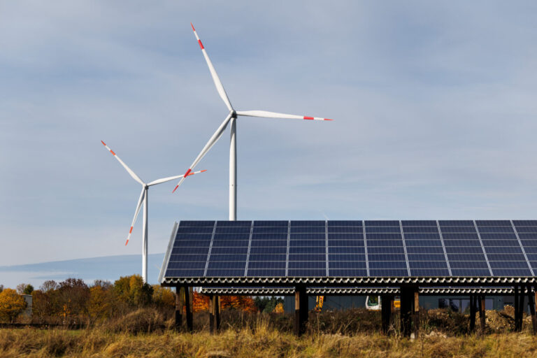 Im Vordergrund sieht man Photovoltaikanlagen, dahinter drehen sich Windräder im Wind – die Stromerzeugung der Energiewende sorgt für Chaos