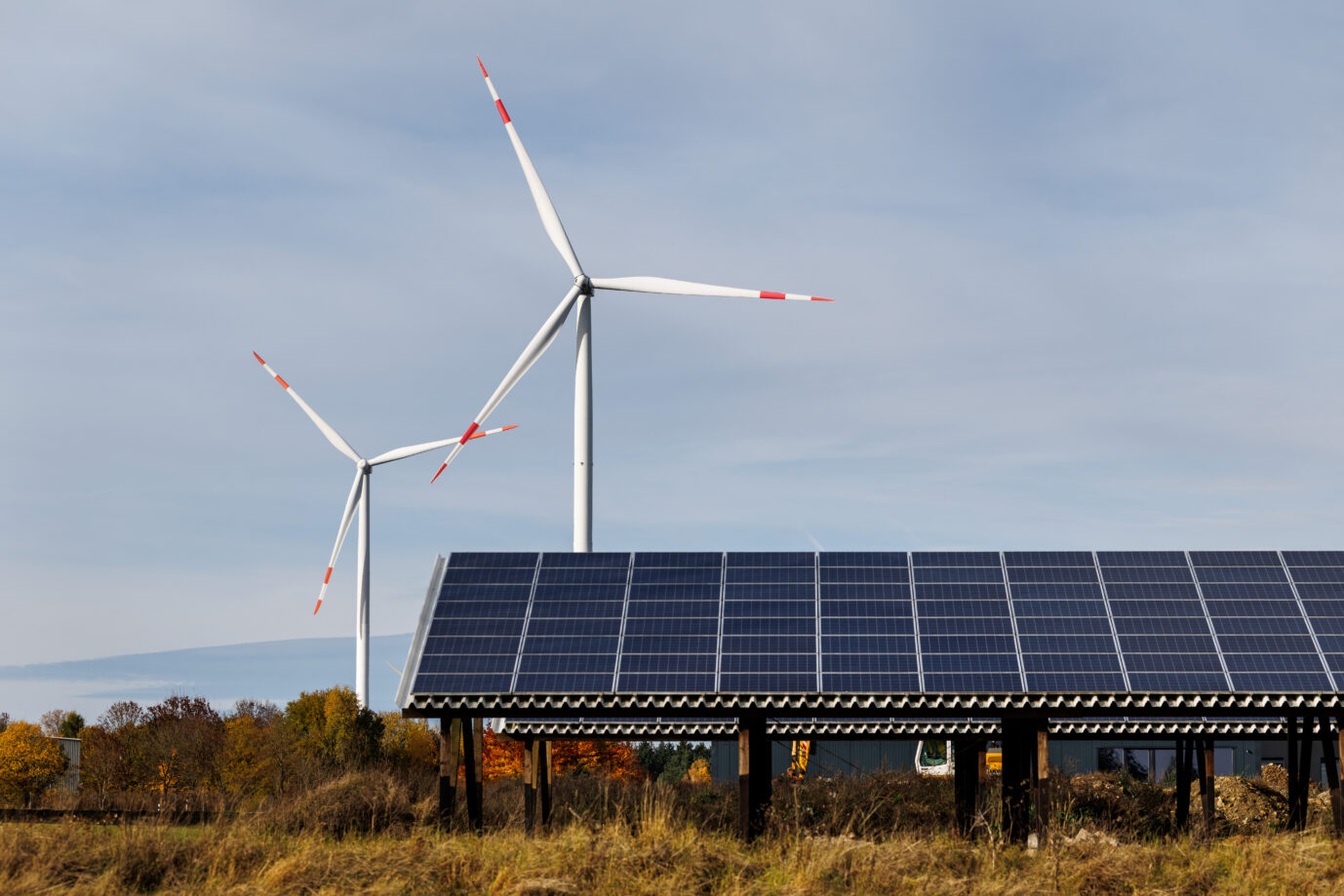 Im Vordergrund sieht man Photovoltaikanlagen, dahinter drehen sich Windräder im Wind – die Stromerzeugung der Energiewende sorgt für Chaos