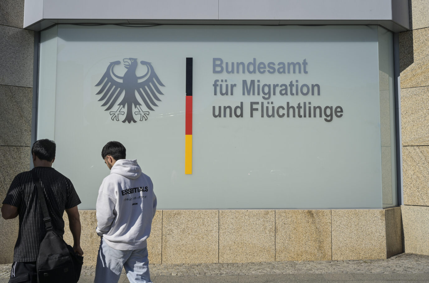 Zwei Männer gehen an einer Außenfassade mit dem Bundesadler und dem Schriftzug Bundesamt für Migration und Flüchtlinge entlang. Symbolfoto zu Migration und Asylverfahren in Deutschland. Vor dem Bundesamt für Migration und Flüchtlinge: Fast eine Million abgelehnte Asylbewerber in Deutschland. Foto: picture alliance / Joko | Joko