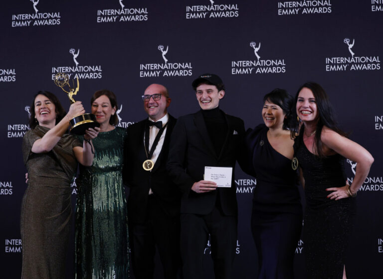 Man sieht eine Gruppe von Menschen freudig strahlend vor einer schwarzen Wand stehen, es ist der deutsche Regisseur Ralf Kukula (dritter von links) und sein Team, die gerade einen International Emmys gewonnen haben