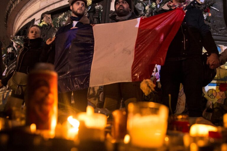 Das Bild zeigt trauernde Menschen mit einer französischen Fahne am Platz der Republik in Paris.