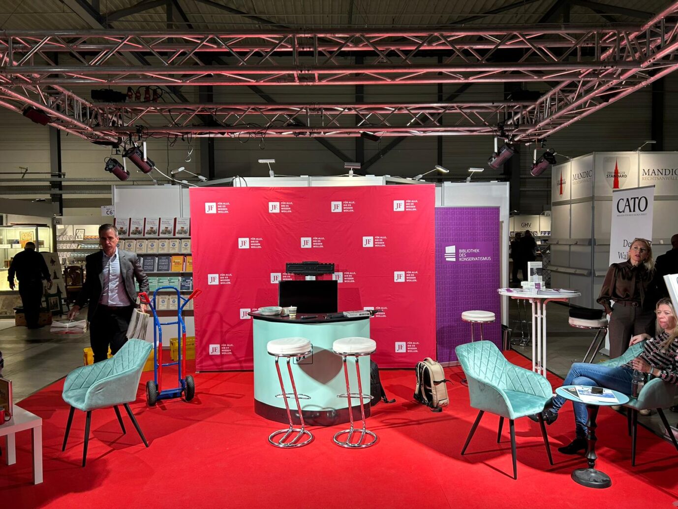 Am Stand der Jungen Freiheit sieht man einen roten Teppich, einen weißen Tisch und ein rotes Banner