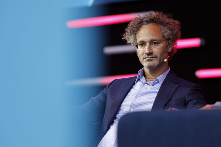 Alex Karp sitzt auf einer Bühne in einem Sessel, trägt Sakko und Hemd und blickt ernst nach vorn, im Hintergrund farbige Lichtstreifen. Palantir-CEO Alex Karp äußert sich im Handelsblatt-Interview kritisch zu Deutschlands technologischem Niedergang und zur Migrationspolitik. Palantir-CEO Alex Karp in Köln: hält nichts von Deutschlands Migrationspolitik. Foto: picture alliance / Geisler-Fotopress | Christoph Hardt/Geisler-Fotopres