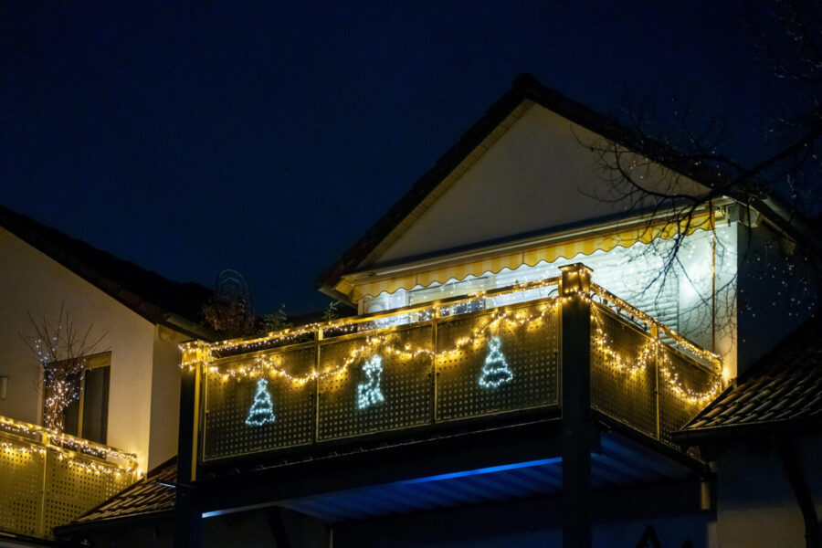 In der Dunkelheit sieht man den Balkon eines Hauses, darauf sind Lichter die thematisch mit Weihnachten in Verbindung stehen