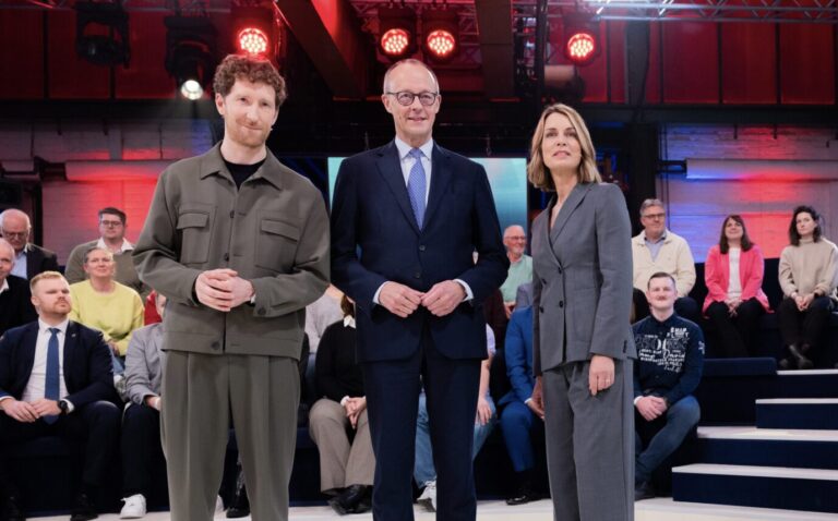 Bundeskanzler Friedrich Merz (M, CDU) steht vor der Live-Sendung ARD-„Arena“ in der Lemo Kulturhalle zusammen mit den Moderatoren Jessy Wellmer und Louis Klamroth (l). Zum Ende seines ersten Jahres im Amt stellt sich der Bundeskanzler in der Sendung live den Fragen von Bürgerinnen und Bürgern.