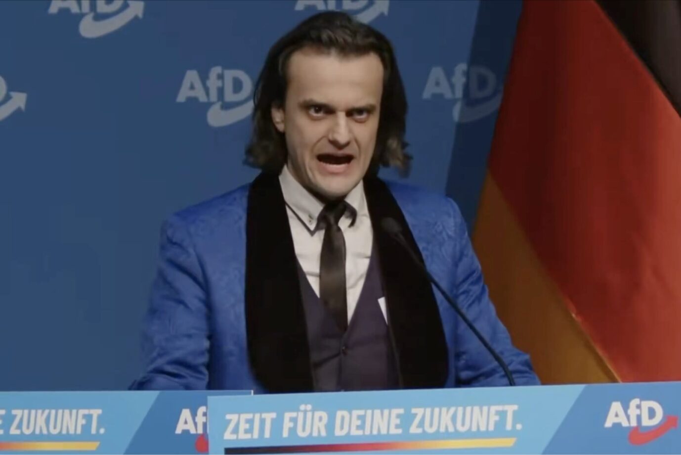 Ein Mann mit schulterlangem Haar verzerrt sein Gesicht zu einer Fratze: Es handelt sich um Alexander Eichwald bei der Gründung der AfD-Jugend in Gießen
