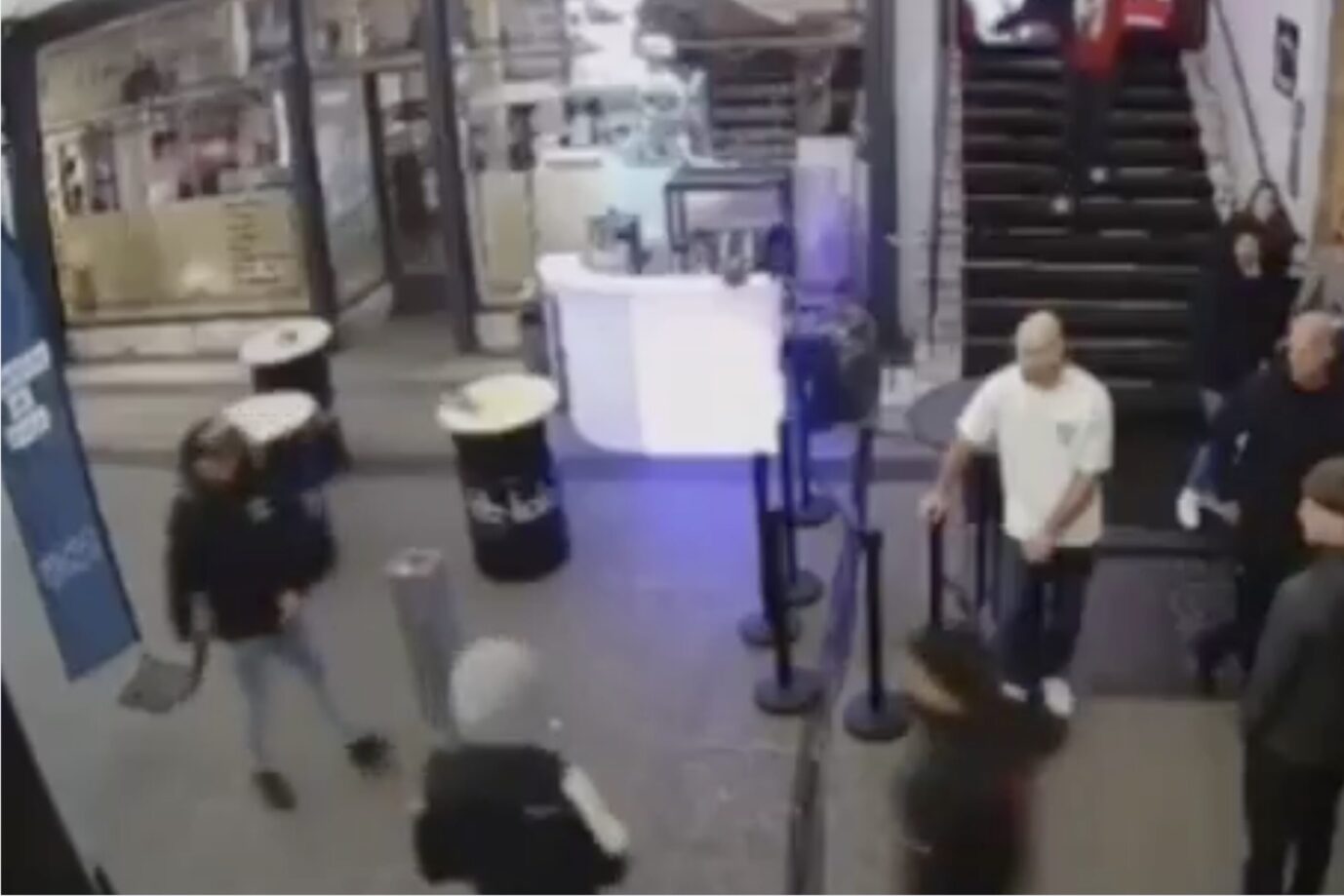 Das pixelige Bild einer Überwachungskamera zeigt mehrere Männer in einer Halle, eine zieht eine Kalaschnikow hervor