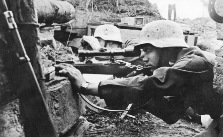 Ein Scharfschütze der Wehrmacht und ein Beobachter beobachten das Gelände.