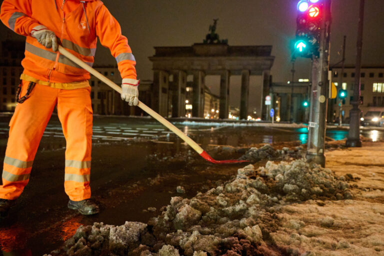 Ein Mitarbeiter der Berliner Stadtreinigung (BSR) schiebt vor dem Brandenburger Tor Schneematsch an den Straßenrand, nachdem es am Vortag geschneit hat.