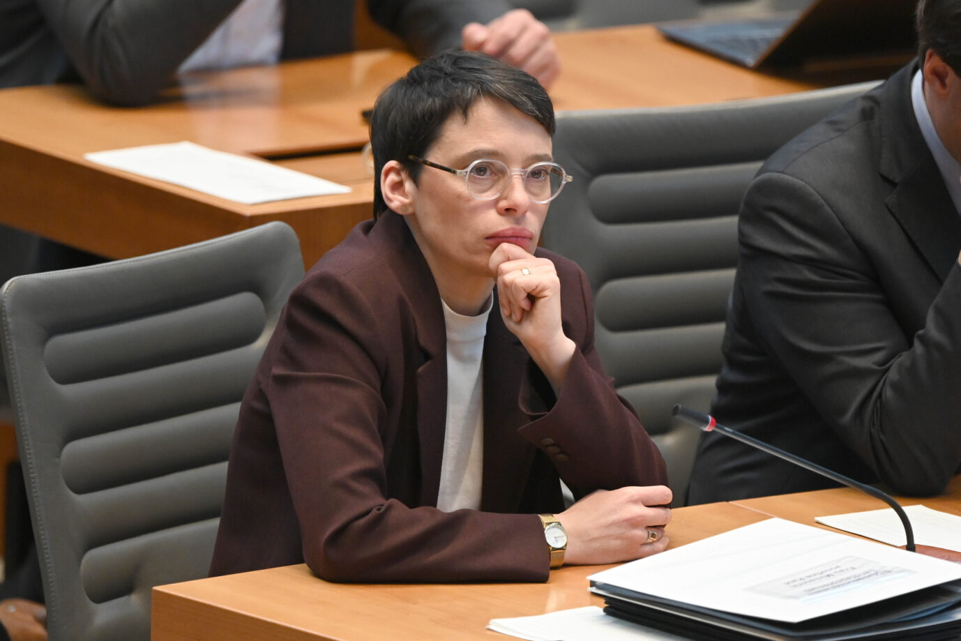 Frau mit Brille und kurzem Haar sitzt nachdenklich an einem Tisch im Landtag, stützt das Kinn auf die Hand, vor ihr liegen Akten und ein Mikrofon. Szene aus dem nordrhein-westfälischen Landtag im Zusammenhang mit der Kritik am Krisenmanagement der damaligen MIgrationsministerin nach dem Solinger Terroranschlag und ihrem späteren Rücktritt. Josefine Paul im Landtag: Ministerpräsident Wüst setzte der Grünen-Politikerin im Zuge der Affäre um zurückgehaltene SMS eine Frist. Foto: picture alliance / SvenSimon | Malte Ossowski/SVEN SIMON