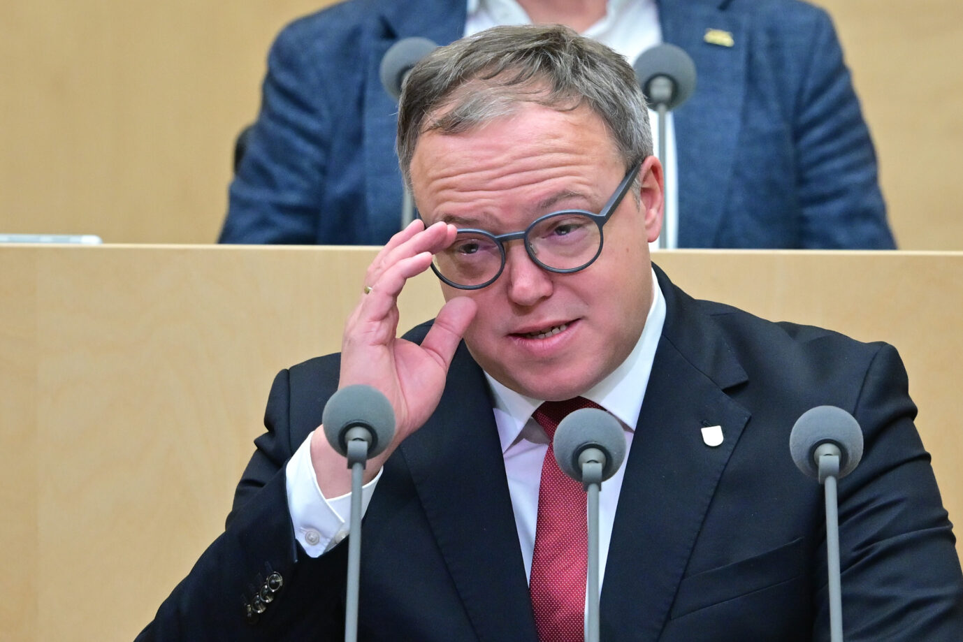 Mario Voigt spricht am Rednerpult im Thüringer Landtag, hebt die Hand an seine Brille und blickt angespannt nach vorn. Hintergrund ist eine Plenarsitzung, vor ihm mehrere Mikrofone. Mario Voigt im Thüringer Landtag: Die TU Chemnitz hat dem Ministerpräsidenten den Doktorgrad aberkannt. Foto: picture alliance/dpa | Sebastian Christoph Gollnow