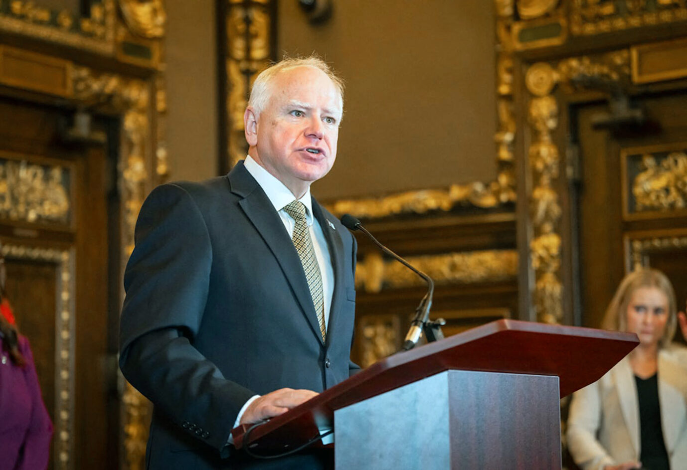 Der Gouverneur Minnesotas, Tim Walz, steht an einem Rednerpult und schaut mit bedrückter Miene drein