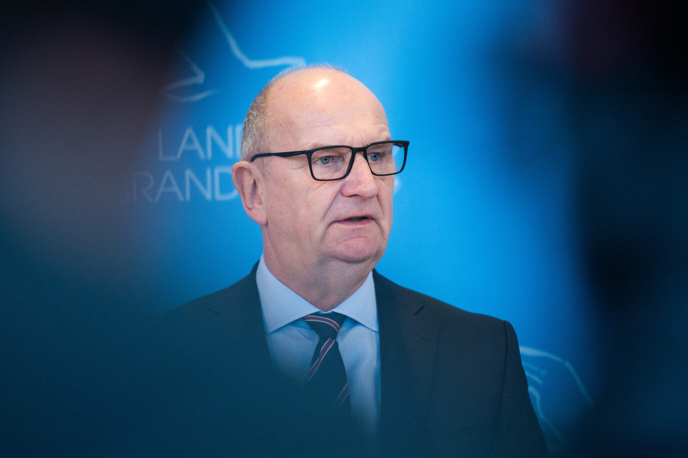 Porträtaufnahme von Dietmar Woidke in dunklem Anzug und Krawatte, stehend vor blauem Hintergrund mit Landesemblem, aufgenommen während eines Statements in der Potsdamer Staatskanzlei. Woidke äußerte sich dort zur Koalitionskrise in Brandenburg und begründete den Bruch der bundesweit einzigen SPD-BSW-Landesregierung mit einer fehlenden Vertrauensbasis. Dietmar Woidke in der Staatskanzlei: Der Ministerpräsident erklärte das Ende der SPD-BSW-Koalition. Foto: picture alliance/dpa | Christophe Gateau