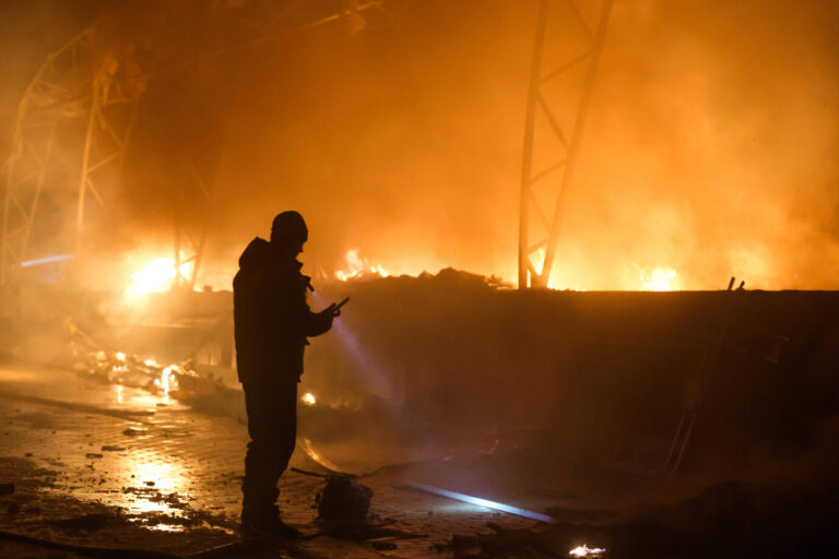 Ein Mann steht vor einem brennenden Gebäude, es handelt sich um ein Bild aus dem Ukraine-Krieg