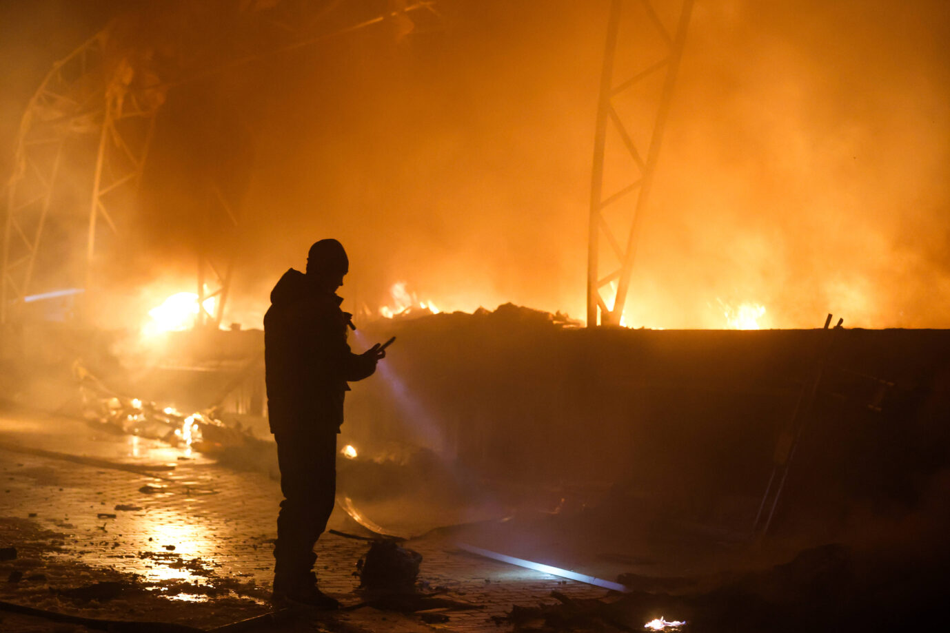Ein Mann steht vor einem brennenden Gebäude, es handelt sich um ein Bild aus dem Ukraine-Krieg